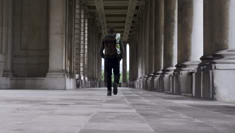 Male-Tourist-With-Backpack-Walking-Past-Colonnade-At-Royal-Navel-College-In-Greenwich