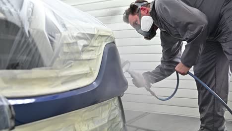 Painter-with-protective-mask-spray-painting-vehicle,-slow-motion-view