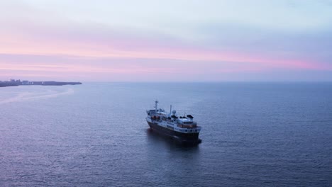Natgeo-passenger-cruise-ship-stationary-in-calm-ocean-water-with-purple-sunset