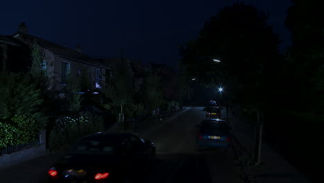 Jib-down-of-car-driving-through-peaceful-suburban-neighborhood-at-night