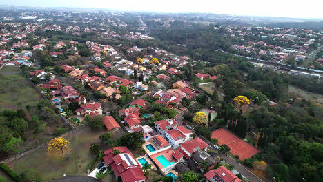 Flyover-suburban-neighborhood,-top-view-of-Houses-rooftops-between-vegetation-with-yellow-tree-spots,-Flying-forward