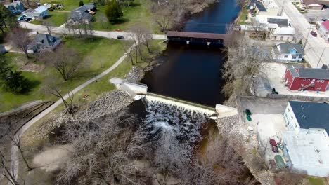 Aerial-fly-over-the-historic-covered-wooden-bridge-over-the-creek-in-a-small-American-town---establishing-shot