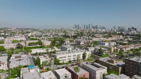 Flight-over-Los-Angeles-on-Sunny-California-Day,-Rooftops-Below-and-City-Skyline-Ahead