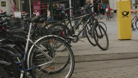 Crowded-bike-rack-near-people-walking-bikes-on-Balvarian-street-in-downtown-Tubingen,-Germany,-Europe,-panning-shot