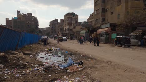 Blick-Aus-Der-Ersten-Person-Auf-Die-Belebte-Lokale-Unbefestigte-Straße-Von-Kairo-Mit-Müll-Und-Ladenfronten-In-Ägypten