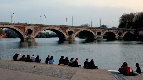 Young-people-enjoying-the-sunset-at-the-Garonne-riverbank-in-front-of-the-Pont-Neuf-bridge