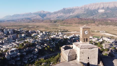 Gjirokaster,-Albania---Reversing-Aerial-of-Cityscape,-Castle,-Clock-Tower-and-Dome