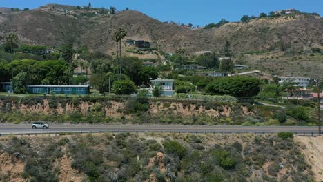 wide-aerial-drone-shot-tracking-cars-parallel-to-the-highway-on-the-hills-of-Malibu-coastline-in-California-during-a-hot-summer-day-in-the-USA