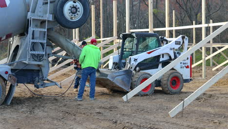 Construction-crew-pouring-wet-cement-into-bucket-of-skid-steer-loader