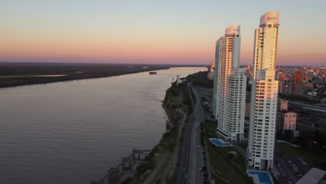 Beautiful-aerial-drone-forwarding-shot-of-Puerto-Norte-Atardecer,-Argentina-along-with-multi-storied-buildings-along-the-coast-of-the-parana-river-with-motor-boats-passing-by-during-evening-sunset