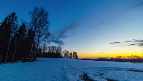 Dramatic-clouds-flying-at-dawn-in-the-morning-with-orange-colored-sunrise-lighting-over-snowy-winter-field