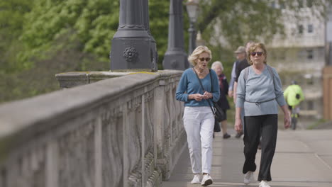 Elder-woman-walking-over-old-stone-bridge-in-Kingston-upon-Thames,-slow-mo-view