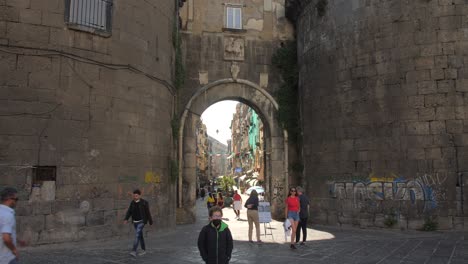 Tilt-down-shot-of-a-historic-entrance-gate-with-locals-passing-by-in-Naples,-Italy-at-daytime