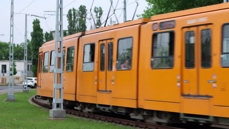 Orange-electric-commuter-train-comes-around-curve-towards,-past-camera