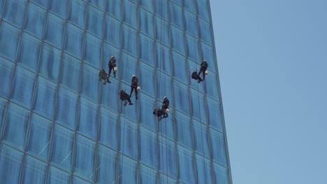Close-up-of-window-cleaners-hanging-and-swinging-from-a-glass-curtain-wall-of-modern-skyscraper,-Santiago-Chile