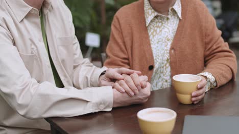 Elderly-couple-holding-hands-while-having-a-cup-of-coffee-outdoors,-romance-love-support-concept