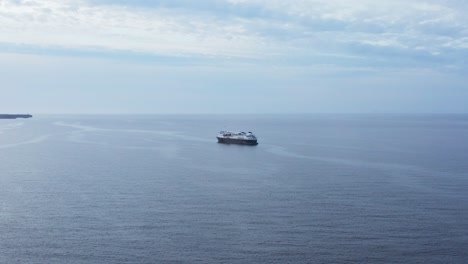 Flying-away-from-anchored-cruise-ship-in-calm-Atlantic-ocean-water,-aerial