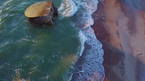 Aerial-birdseye-view-of-abandoned-seaside-fortification-buildings-at-Karosta-Northern-Forts-on-the-beach-of-Baltic-sea-,-waves-splash,-golden-hour-sunset,-drone-shot-moving-forward