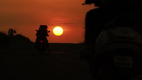 Low-back-view-of-motorcycle-driving-on-the-road-during-sunset-time-in-India-at-Diu-city