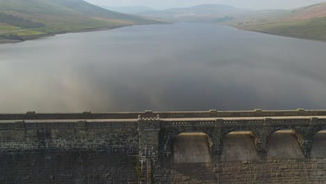 Pull-out-aerial-over-the-dam-at-Scar-House-Reservoir-Yorkshire,-England