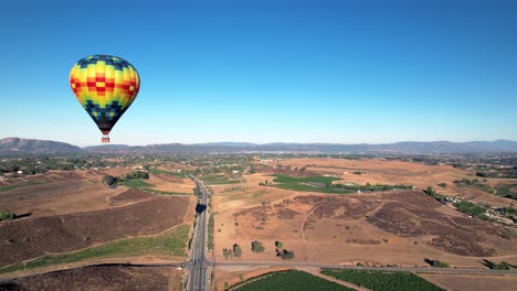 Flying-by-a-hot-air-balloon-floating-over-the-Temecula-vineyards-in-Southern-California,-aerial