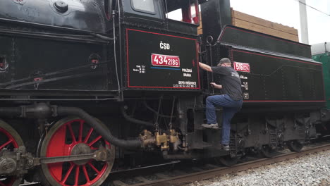 Train-conductor-climbing-into-steam-locomotive-cabin-to-drive-it