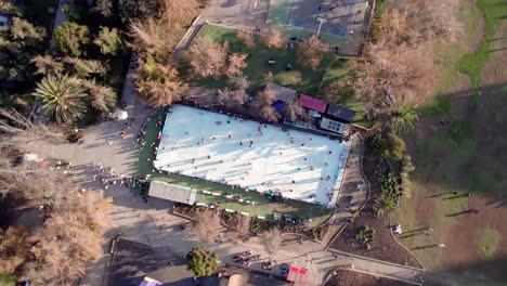 Overhead-spiral-boom-up-view-of-an-ice-skating-rink-with-people,-Parque-Araucano,-Santiago,-Chile