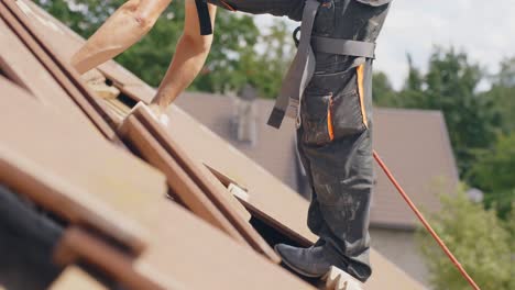 Man-working-on-roof-with-safety-rope,-removing-nails-from-tiles