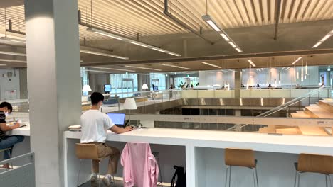 Panning-shot-showing-korean-students-with-face-mask-sitting-on-modern-library-building-with-laptop---working-and-learning-inside-Asia-Culture-Center-of-Gwangju