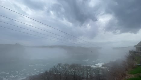 Niagara-falls-zip-line-going-through-mist-along-Niagara-river-foggy-day,-wide