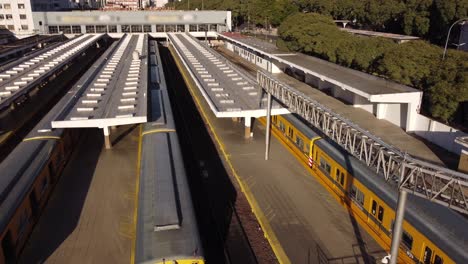 Birds-eye-forward-view-of-yellow-train-arriving-at-Federico-Lacroze-station-of-Buenos-Aires-in-Argentina