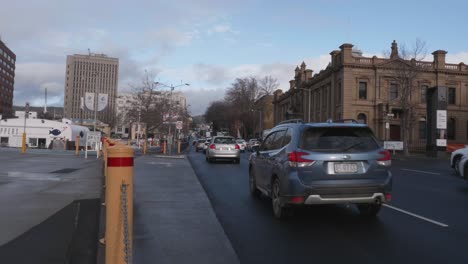Traffic-drives-down-Davey-Street-on-wet-road,-surrounded-by-sandstone-and-office-buidlings-in-Hobart,-Tasmania,-Australia