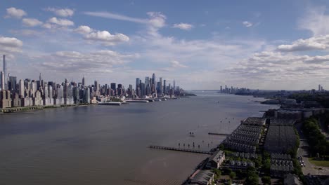 Aerial-view-overlooking-the-West-New-York-coastline-with-Manhattan-background,-in-sunny-New-Jersey,-USA---rotating,-pull-back,-drone-shot
