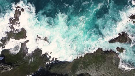 Static-overhead-shot-of-strong-sea-waves-of-Indian-Ocean-hitting-boulder-and-coral-reef-in-the-beach-in-sunny-condition-weather---Pengilon-Hill,-Indonesia,-Asia