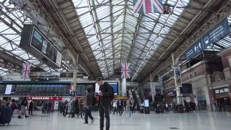 Inside-View-Looking-Up-Roof-Of-London-Victoria-Station-With-Commuters-Walking-Past