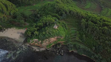 Aerial-top-down-shot-showing-old-building-on-hilltop-with-cliff,ocean-and-private-sandy-beach