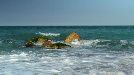 Kleine-Wellen-Schlagen-über-Einige-Felsen-Direkt-An-Einem-Sandstrand-Am-Mittelmeer