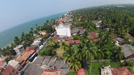 Fpv-Volando-Sobre-Una-Zona-Residencial-Cubierta-De-Palmeras-Verdes-Cerca-Del-Océano-Azul,-Sri-Lanka