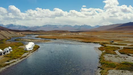 Aerial-drone-flying-past-luxury-glamping-tents-along-an-empty-natural-river-in-the-high-altitude-alpine-plain-of-Deosai-National-Park-located-between-Skardu-and-Astore-Valley-in-Pakistan-while-sunny