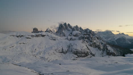 Establishing-aerial-view-across-snow-covered-white-landscape-and-Tre-Cime-majestic-mountain-peaks-in-the-distance