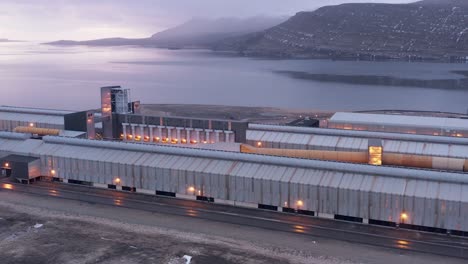 Industrial-building-on-shore-of-scenic-fjord-during-cloudy-morning,-aerial
