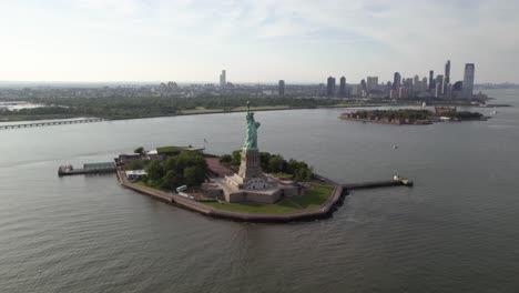 Lady-Liberty-statue-and-island,-in-sunny-New-York,-USA---rising,-tilt-Aerial