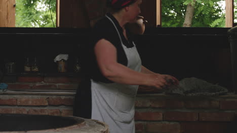 Woman-In-Apron-Pours-Out-Ashes-On-Traditional-Tone-Oven