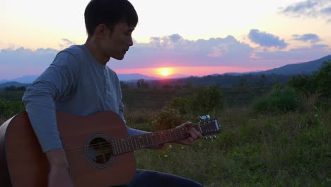 Nahaufnahme-Eines-Asiatischen-Mannes,-Der-Bei-Sonnenuntergang-Und-Horizont-Im-Hintergrund-Gitarre-Spielt,-Vietnam