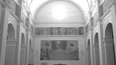 Beautiful-tilting-shot-of-the-aisle,-ceiling,-and-interior-of-famous-Santa-Maria-del-Monte-in-black-and-white-in-Cesena,-Italy