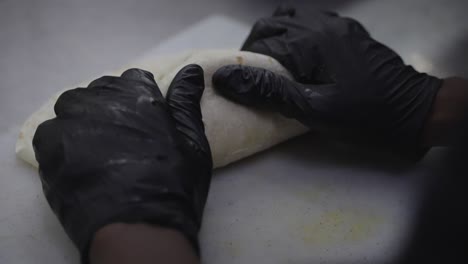 Folding-chicken-wrap-in-close-up,-chef-hands-in-black-gloves
