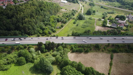 Aerial-Tracking-View-of-Heavy-Cars-Traffic-on-Multi-Lanes-Countryside-Highway,-Surrounded-by-Green-Lands-Trees-and-Suburban-Homes-in-Gdynia-Poland