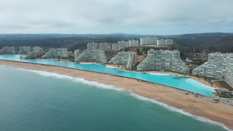 Aerial-of-turquoise-world-largest-swimming-pool-near-sea,-sand-beach-and-luxurious-resorts-in-Algarrobo,-Chile