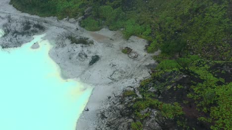 withered-trees-on-a-beach-surrounded-by-a-blue-sulfur-lake-in-Kawah-Putih-in-Bandung-Indonesia,-aerial