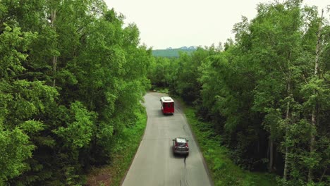 Fahrzeuge-Fahren-Durch-Eine-Schmale-Straße-Zwischen-Einem-Dichten-Grünen-Wald---Luftaufnahme-In-Zeitlupe